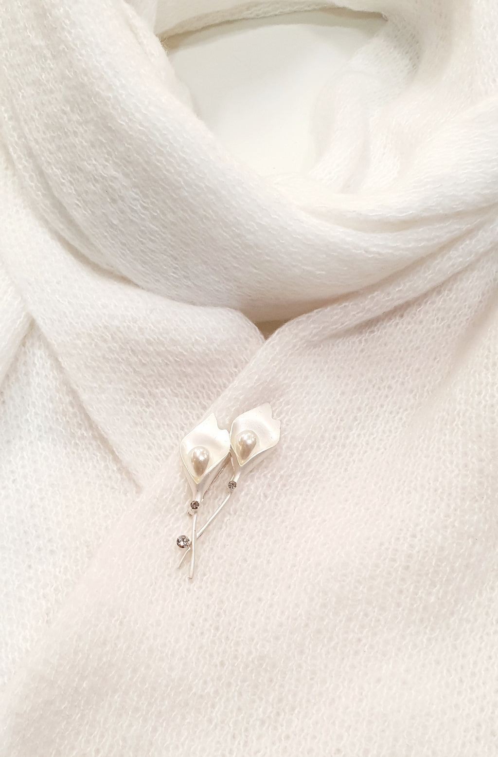 De Calliane is een verfijnde speldbroche geïnspireerd op de elegantie van de Calla-lelie.

De bloemvormige lijnen in zilver en wit worden verfijnd afgewerkt met kunststof parels en heldere kristallen, die het licht subtiel vangen.
Haar tijdloze ontwerp straalt rust en stijl uit — perfect voor sjaals, blazers of feestelijke gelegenheden.