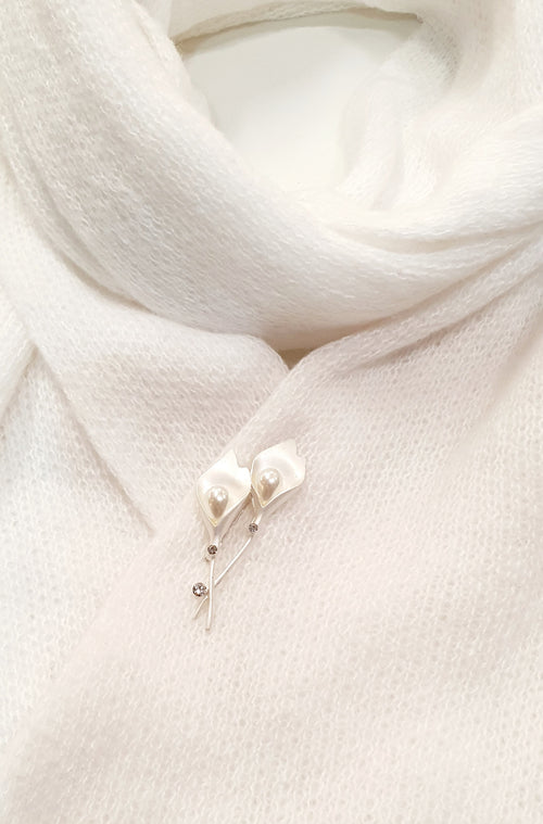 De Calliane is een verfijnde speldbroche geïnspireerd op de elegantie van de Calla-lelie.

De bloemvormige lijnen in zilver en wit worden verfijnd afgewerkt met kunststof parels en heldere kristallen, die het licht subtiel vangen.
Haar tijdloze ontwerp straalt rust en stijl uit — perfect voor sjaals, blazers of feestelijke gelegenheden.
