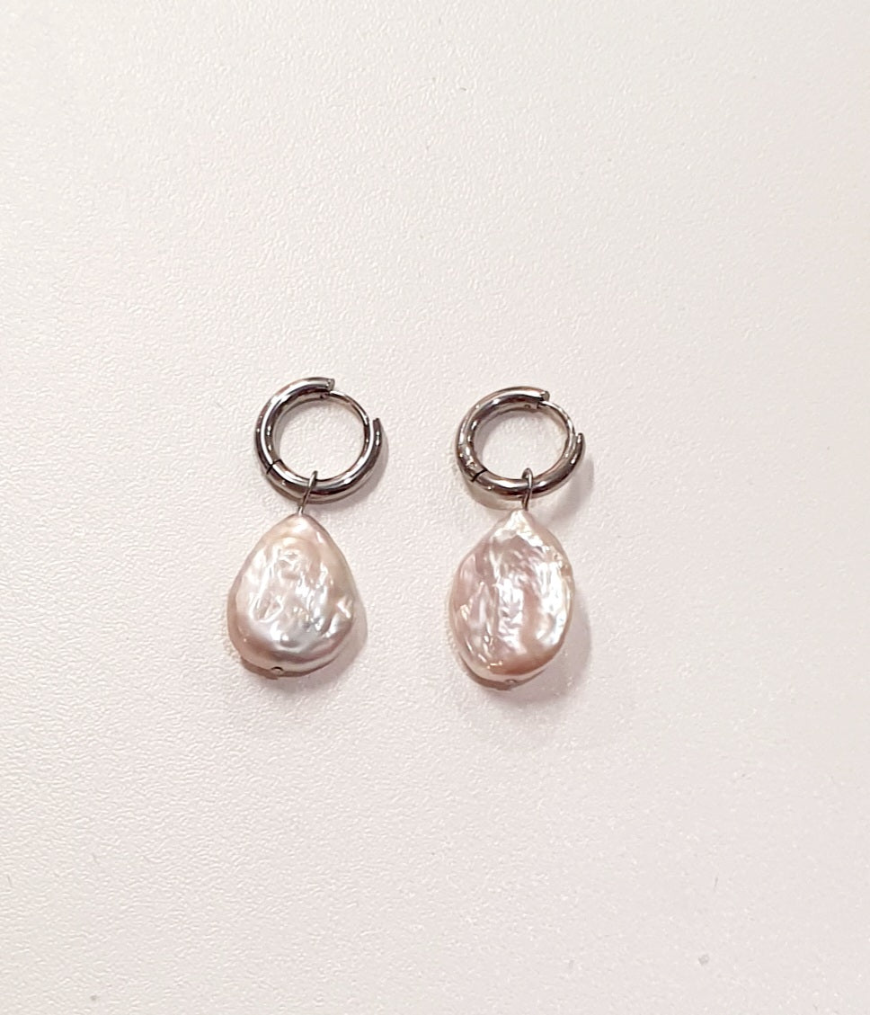 De JES Original Princess Barok is een ode aan natuurlijke elegantie en vrouwelijke kracht.
Deze artisanale zoetwaterparel set werd met de hand samengesteld uit zorgvuldig geselecteerde parels, elk met een eigen vorm, glans en karakter. Geen twee parels zijn identiek — precies daarin schuilt haar schoonheid.


De ketting bestaat uit 68 echte zoetwaterparels, harmonieus geregen tot een verfijnde streng. Centraal hangt een barokke parel, puur en expressief, die afneembaar is via een discreet slotje. Zo draagt 